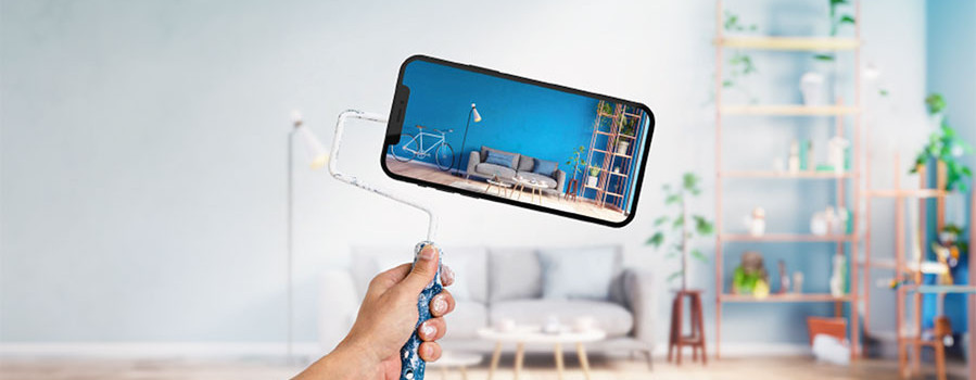 Person hält Farbrolle mit Handy als Rolle in Wohnzimmer – auf dem Handy das umgestaltete Wohnzimmer sichtbar. Spectrum Anwendung.